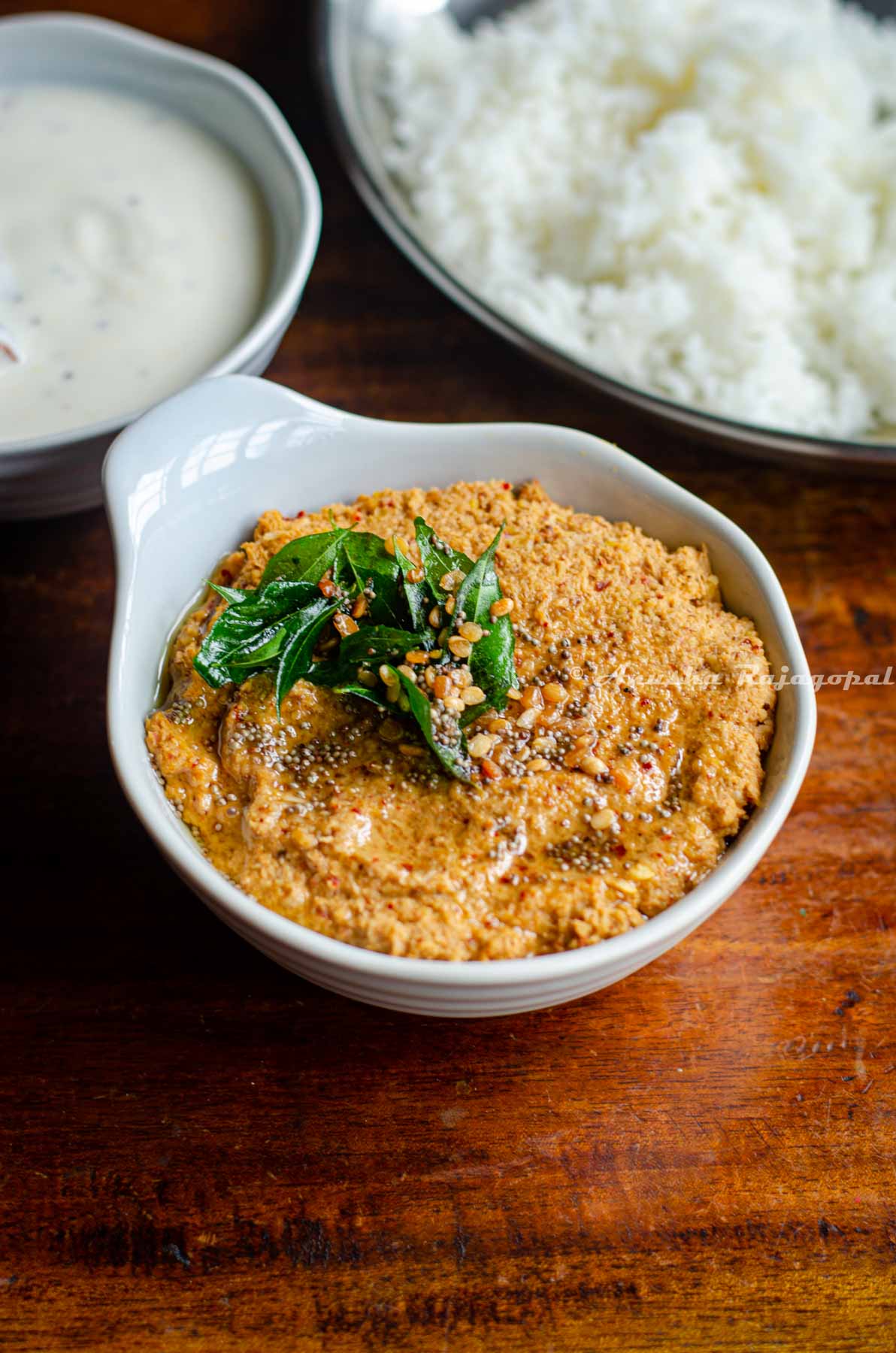 traditional South Indian style Paruppu thogayal served in a white bowl placed over a wooden table. A tempering has been added to the Thogayal