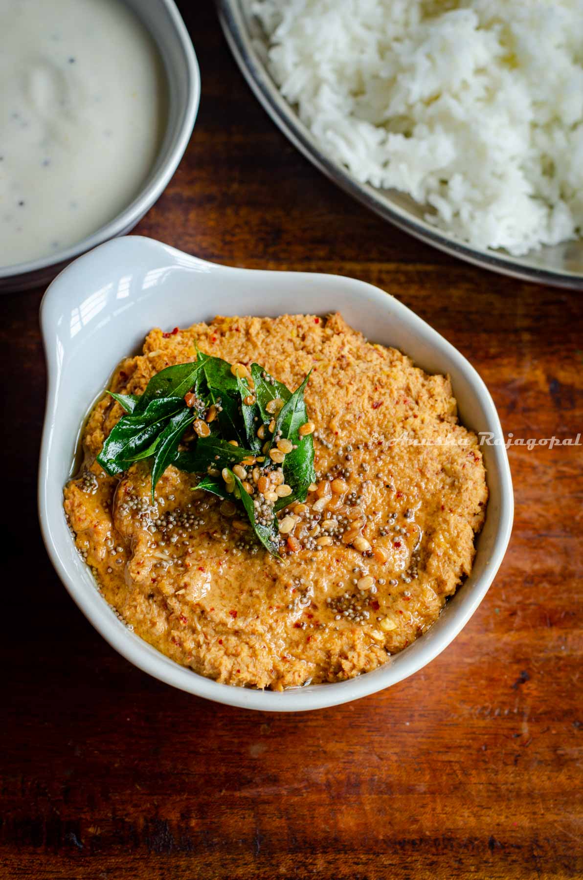 traditional South Indian style Paruppu thogayal served in a white bowl placed over a wooden table. A tempering has been added to the Thogayal