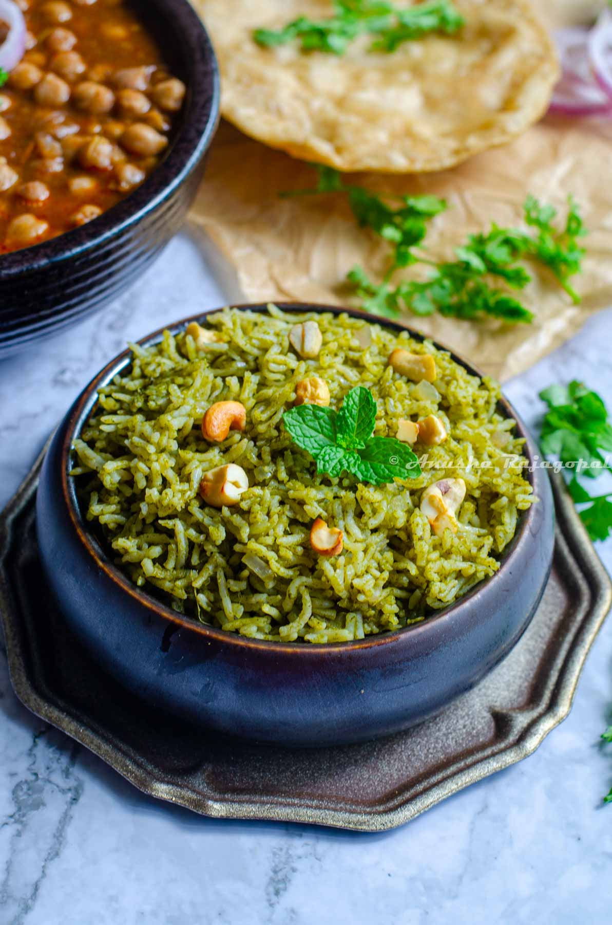 Pudina rice served in a black bowl placed on a metal tray. Cilantro leaves by the side and chole at the far upper left corner.