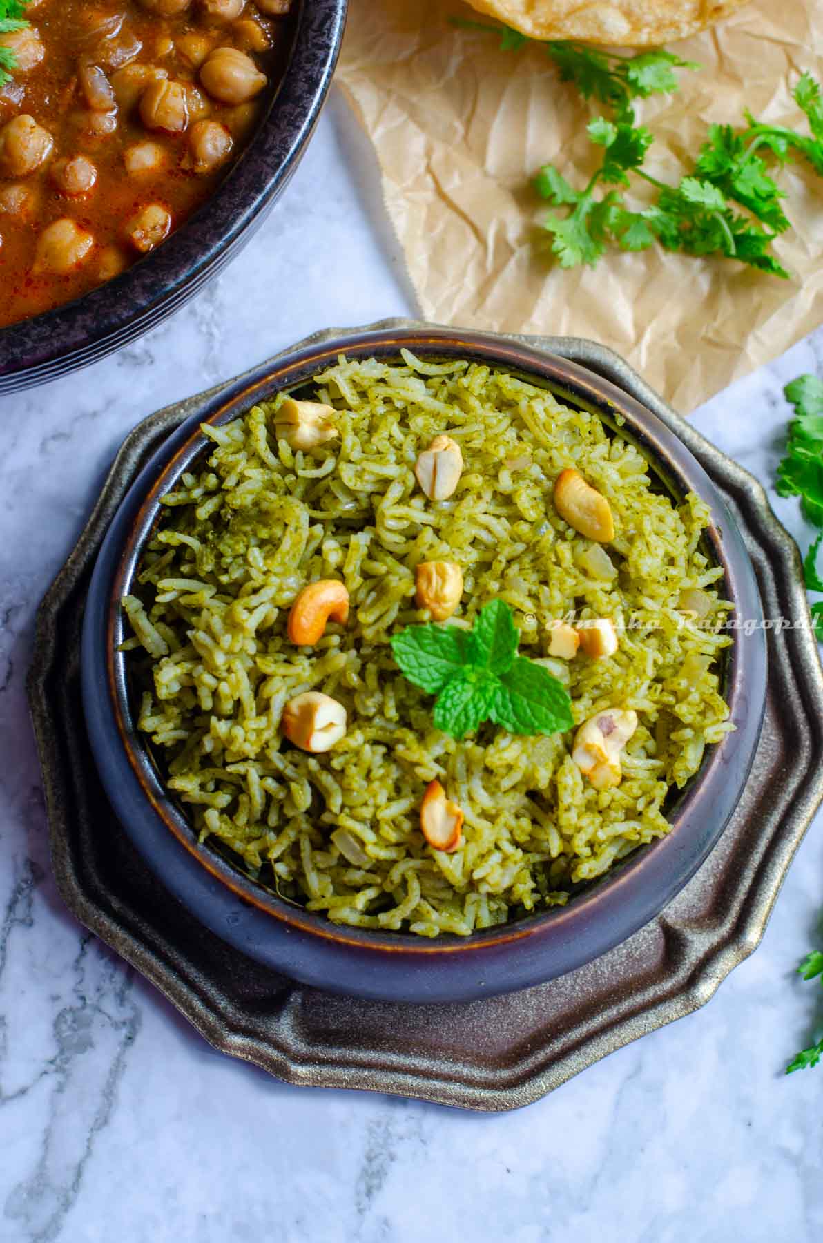 Pudina rice served in a black bowl placed on a metal tray. Cilantro leaves by the side and chole at the far upper left corner.