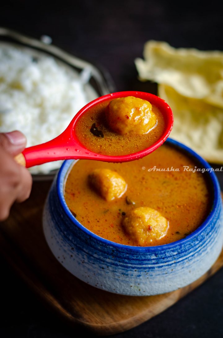 paruppu urundai kuzhambu- South Indian lentil ball gravy served in a white blue bowl.