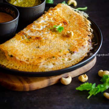 crispy Instant rava dosa served with chutney by the side on a black plate. Coriander leaves and cashews sprinkled on the top and by the side.