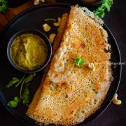 crispy Instant rava dosa served with chutney by the side on a black plate. Coriander leaves and cashews sprinkled on the top and by the side.