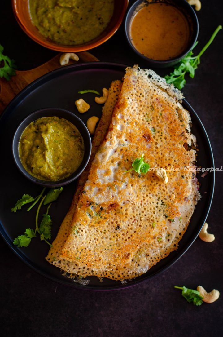 crispy Instant rava dosa served with chutney by the side on a black plate. Coriander leaves and cashews sprinkled on the top and by the side.