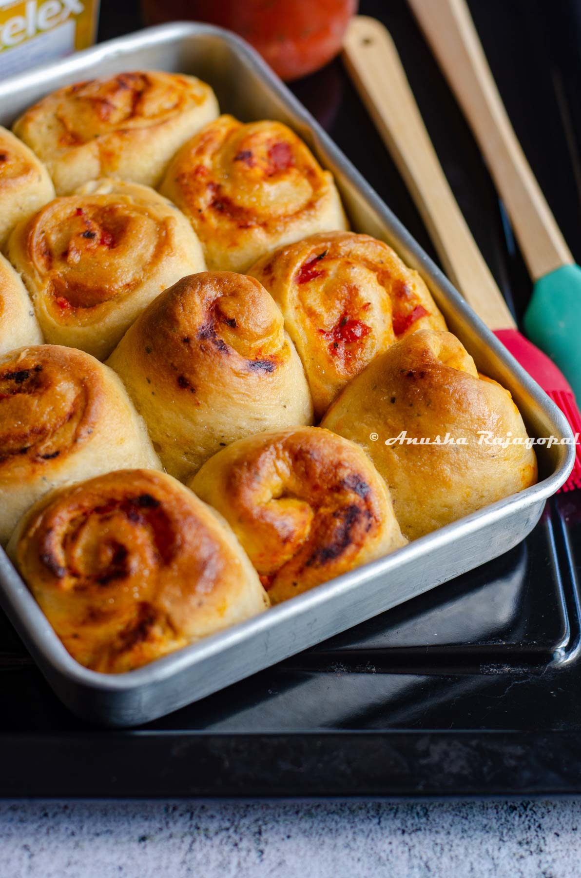 freshly baked pull apart bread with pasta sauce filling in a rectangle shaped baking tray. Spatulas by the side.