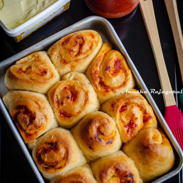 freshly baked pull apart rolls filled with store bought pasta sauce in a baking tray. Spatulas, a jar of sauce and some vegan butter by the side.
