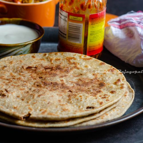 Rajma cheese paratha served on a wooden plate with capsicum zunka, pickles and yogurt by the side.