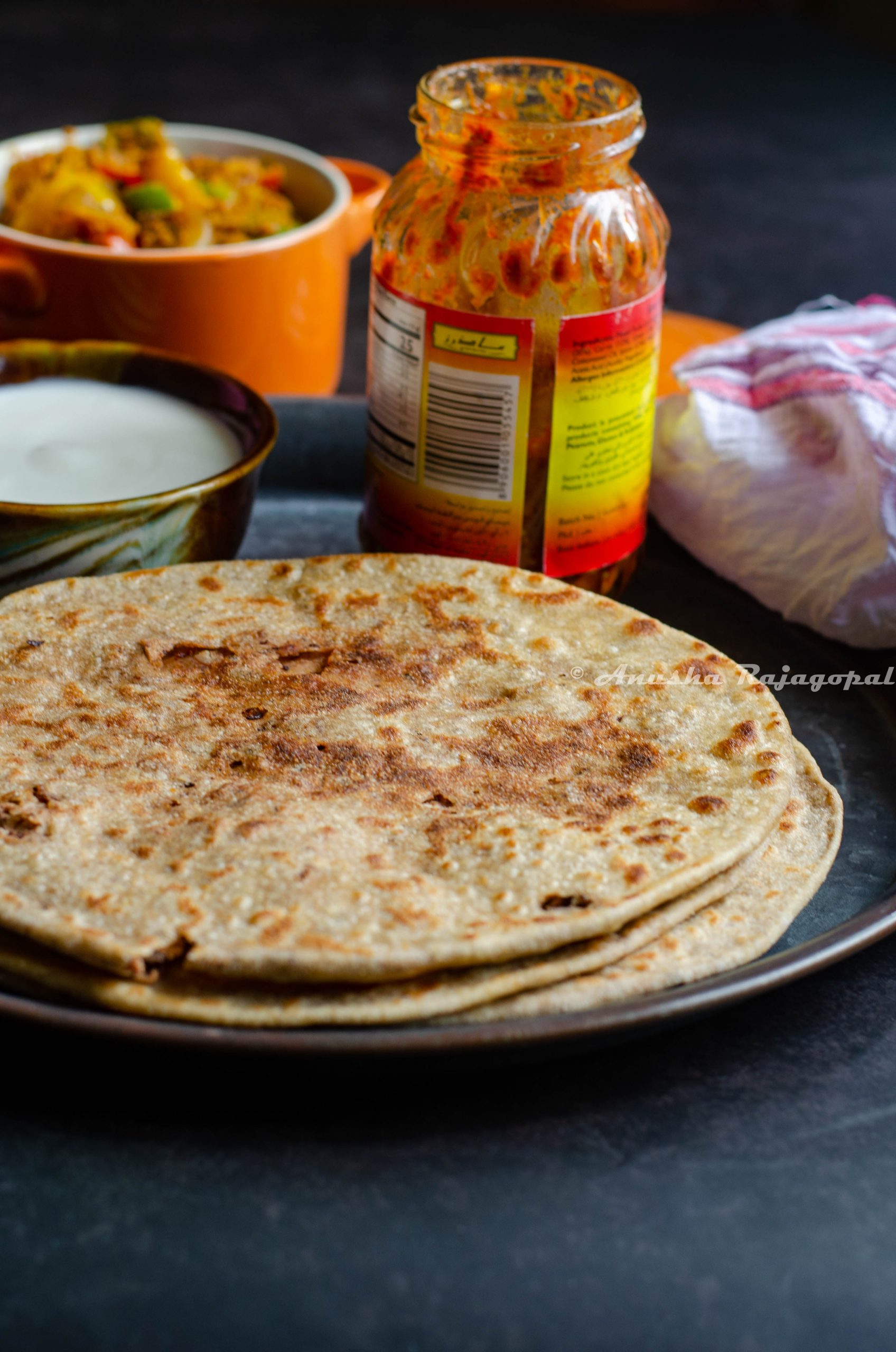 Rajma cheese paratha served on a wooden plate with capsicum zunka, pickles and yogurt by the side.