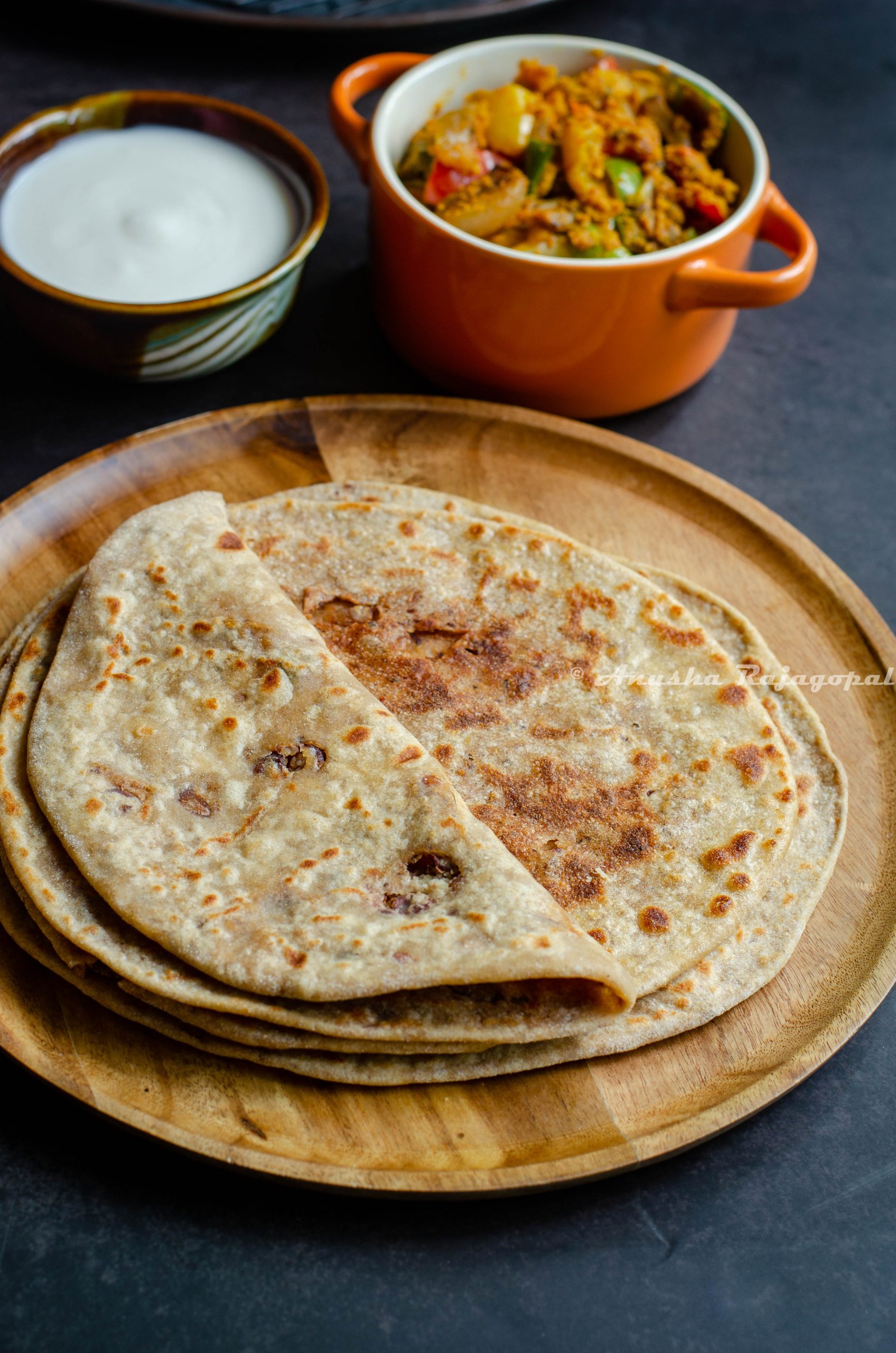 Rajma cheese paratha served on a wooden plate with capsicum zunka, pickles and yogurt by the side.