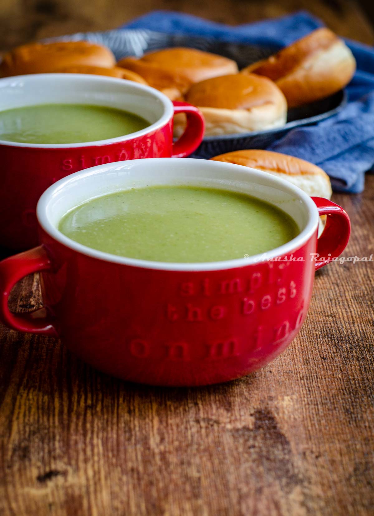 vegan broccoli almond soup served in a red soup bowl with a rolls at the back.