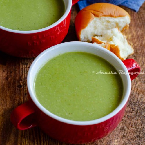 vegan broccoli almond soup served in a red soup bowl with a half eaten roll at the back.