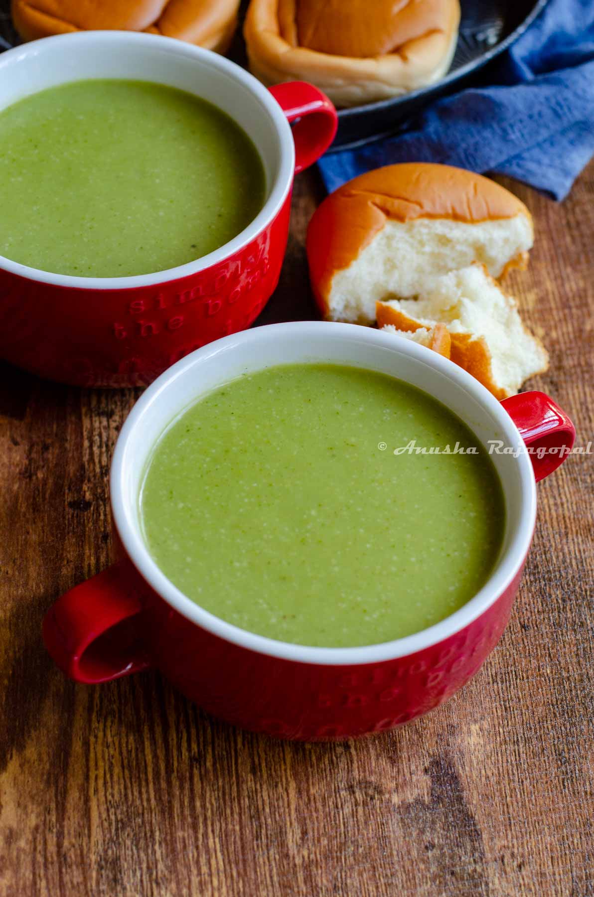 vegan broccoli almond soup served in a red soup bowl with a half eaten roll at the back.