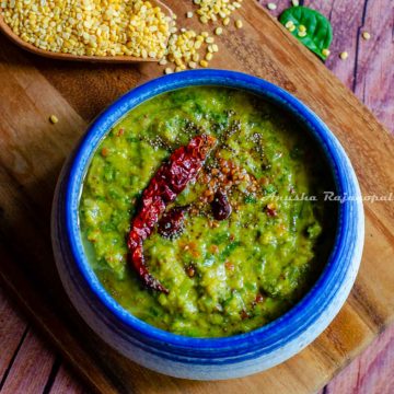 keerai kootu served in a white and blue bowl placed over a wooden chopping board. Moong lentils and spinach leaves by the side.