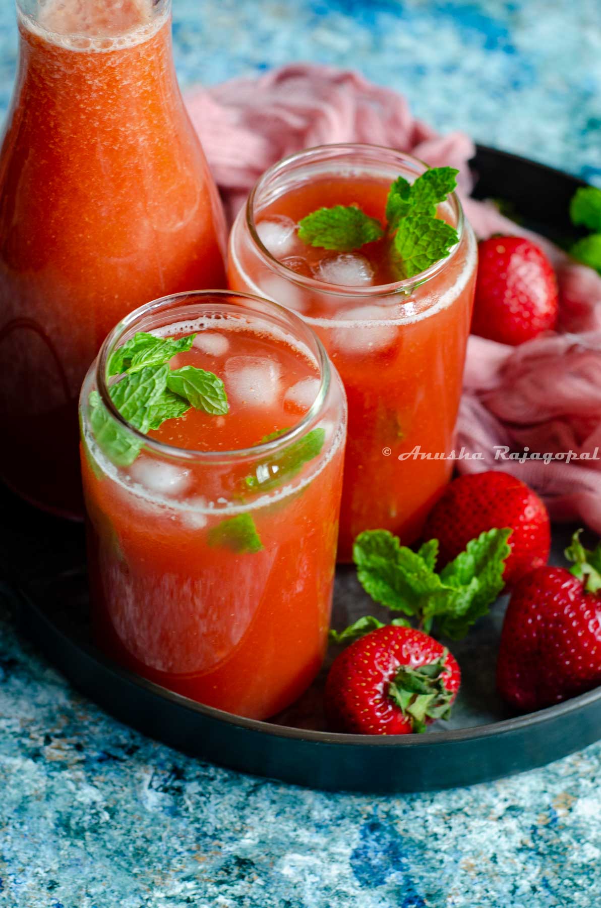 easy pink lemonade served in two tin can style glasses with fresh strawberries around them.