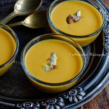 Instant pot carrot kheer served in glass bowls placed over a metallic tray. Kheer is topped with chopped almonds. brass spoons by the side