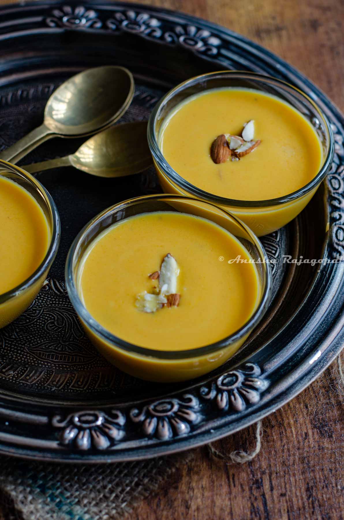 Instant pot carrot kheer served in glass bowls placed over a metallic tray. Kheer is topped with chopped almonds. brass spoons by the side