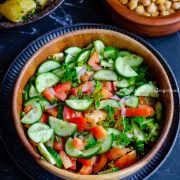 Persian Shirazi salad served in a wooden salad bowl placed over a metal serving platter. Hummus Balila, Batata Harra at the background