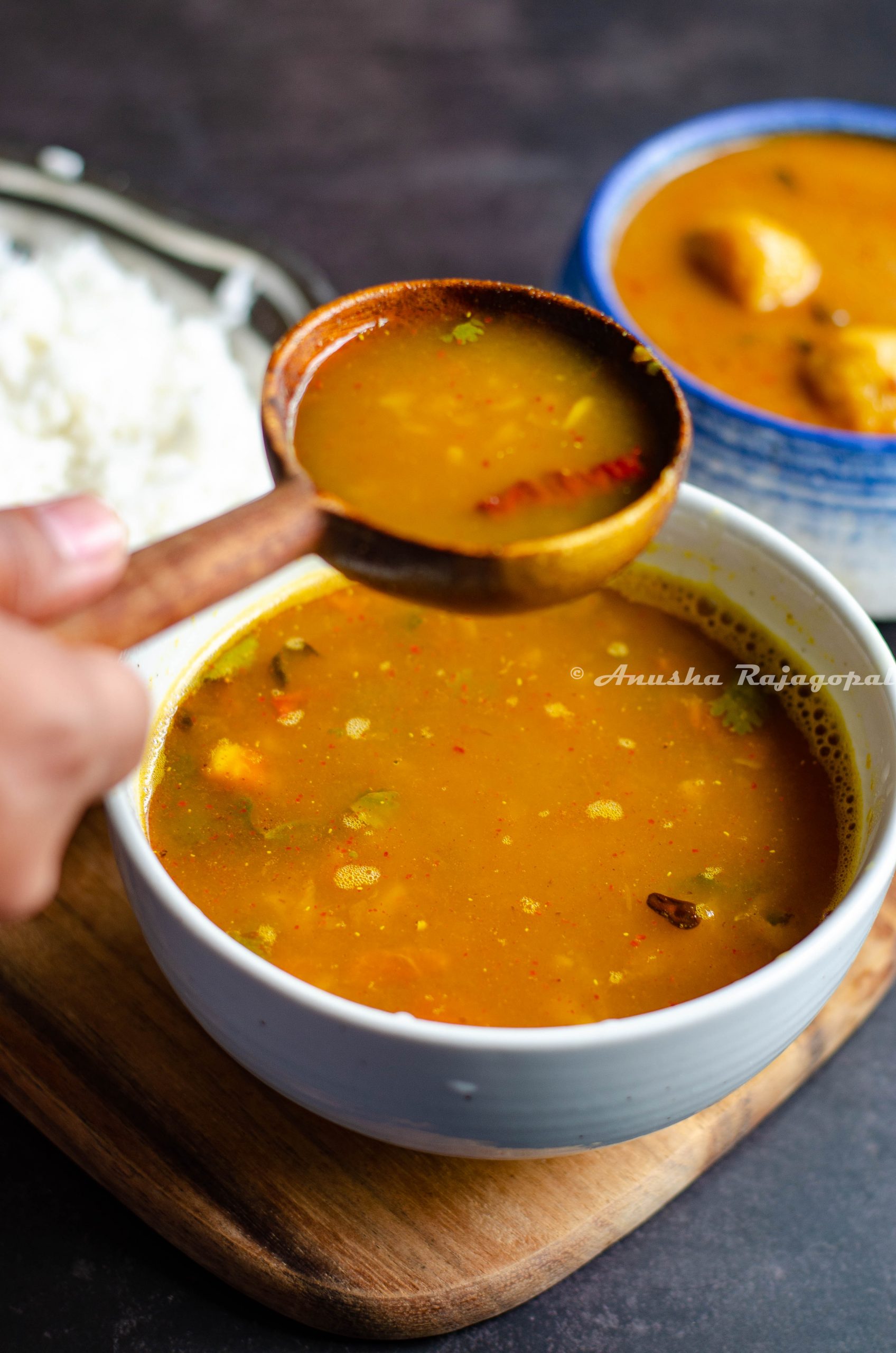 A ladle full of pineapple rasam held over a bowl of rasam