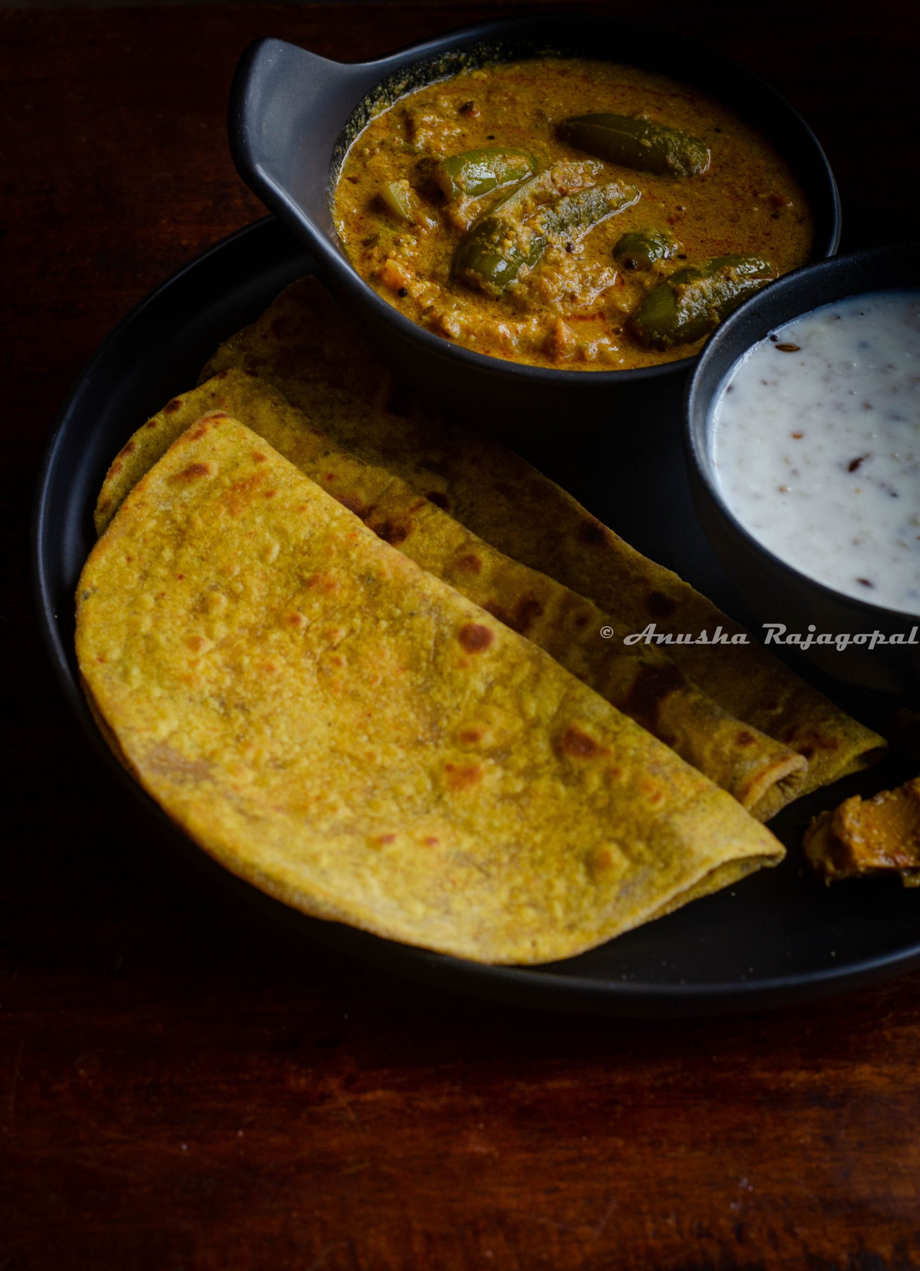 avocado parathas served on a black plate with yogurt and millet in a bowl by the side.