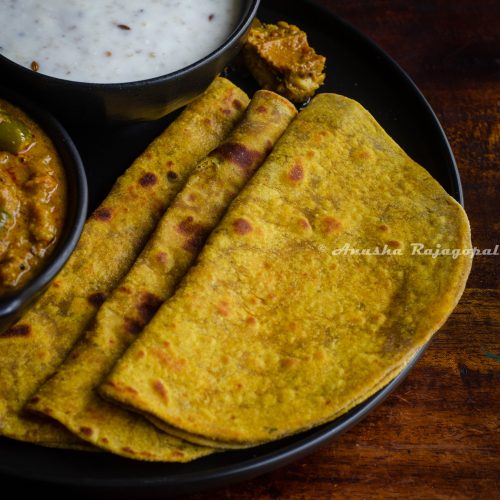 avocado parathas served on a black plate with yogurt and millet in a bowl by the side.
