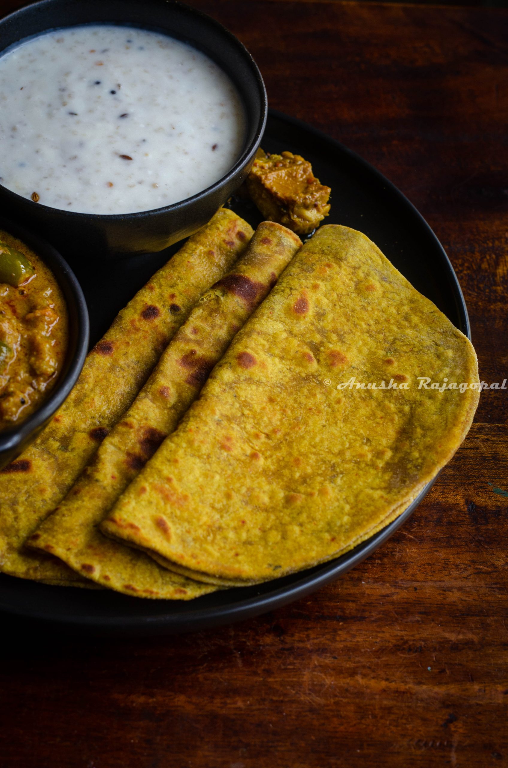 avocado parathas served on a black plate with yogurt and millet in a bowl by the side.