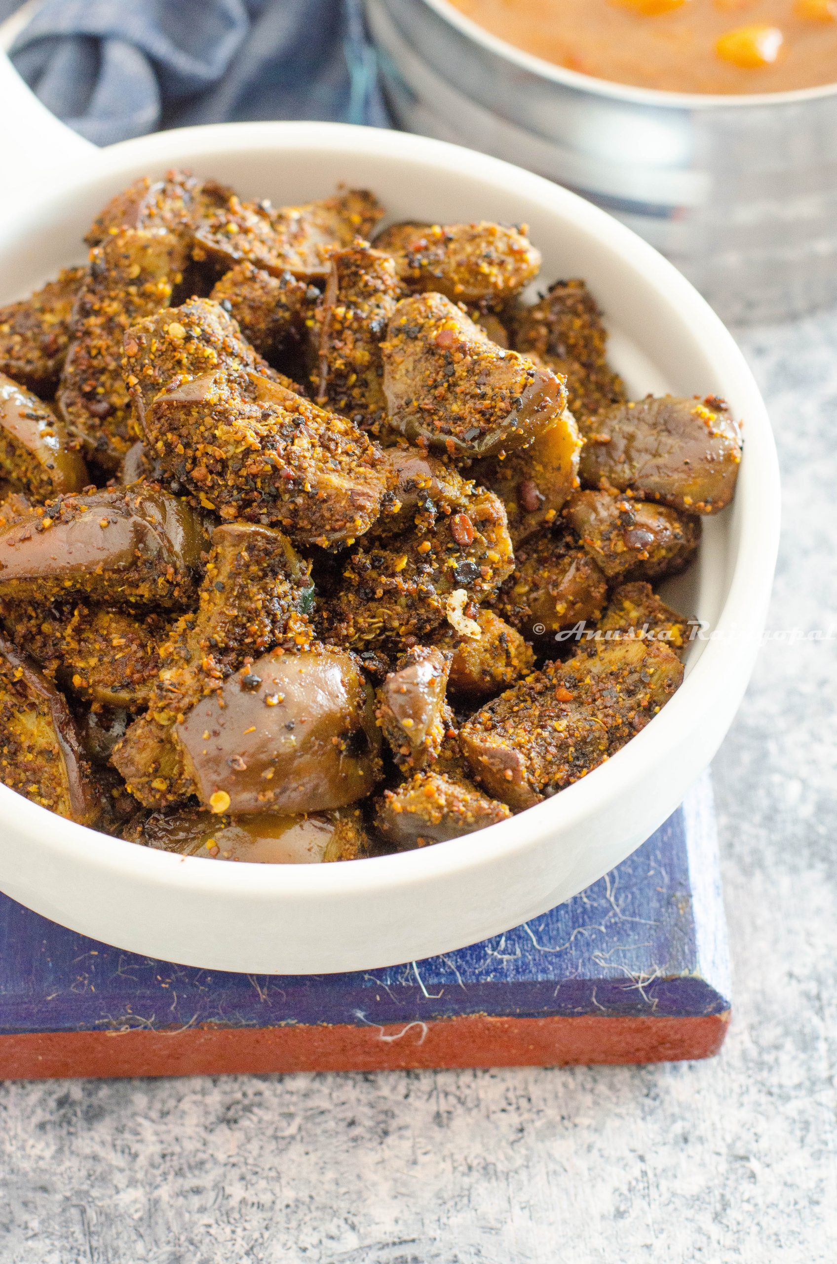 kathrikai podi curry- brinjal stir fry made with fresh spice powder served in a white shallow handled bowl placed on a blue coaster