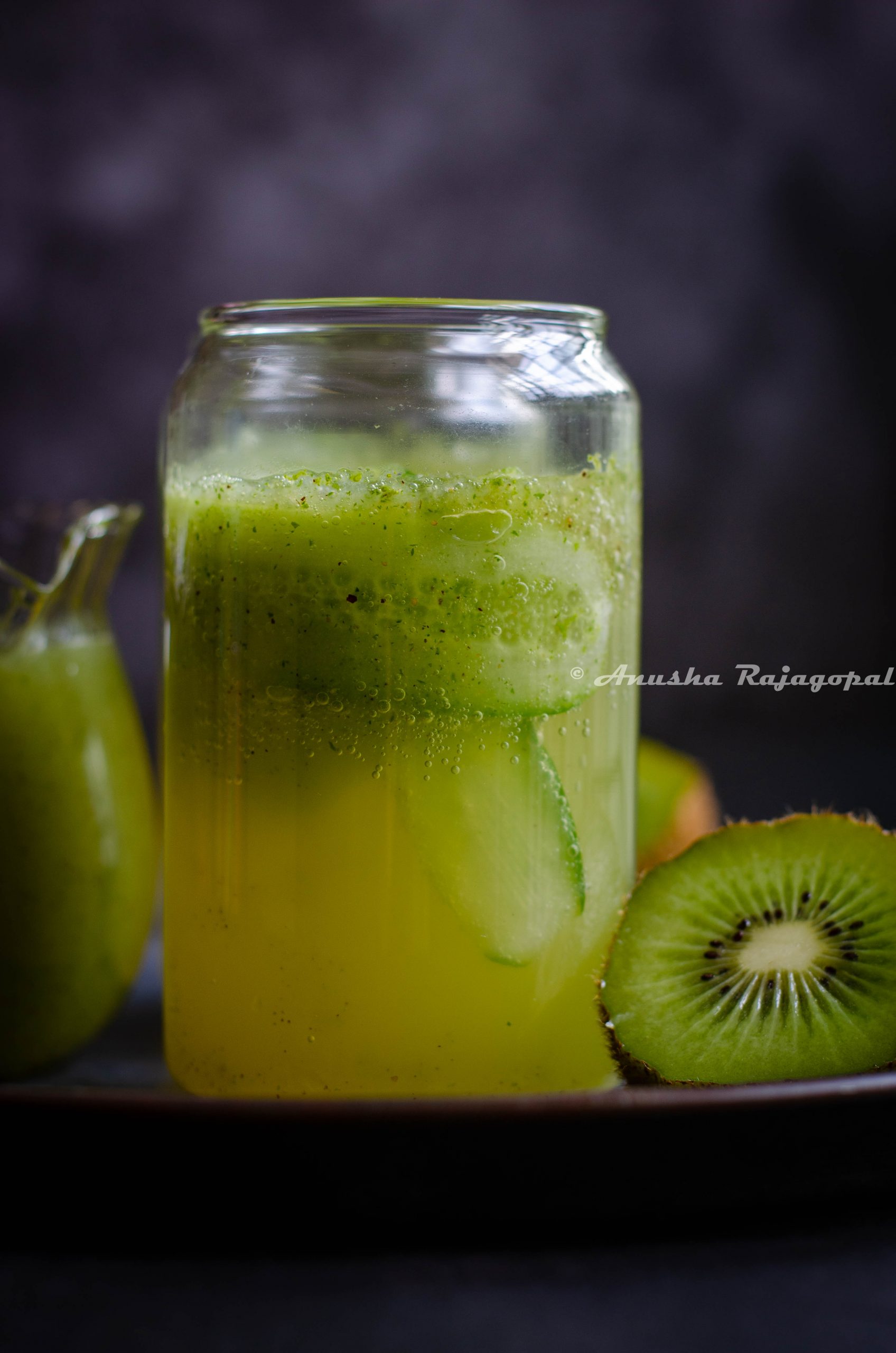 Kiwi cucumber lemonade with cucumber ribbons served in a tall glass against a black backdrop.