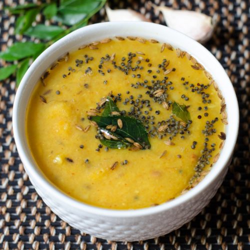 andhra dosakaya pappu tempered with whole spices and curry leaves served in a white bowl.