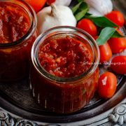 South Indian thakkali thokku- a tangy tomato relish in a glass jar with cherry tomatoes, garlic and curry leaves all presented in a rustic platter