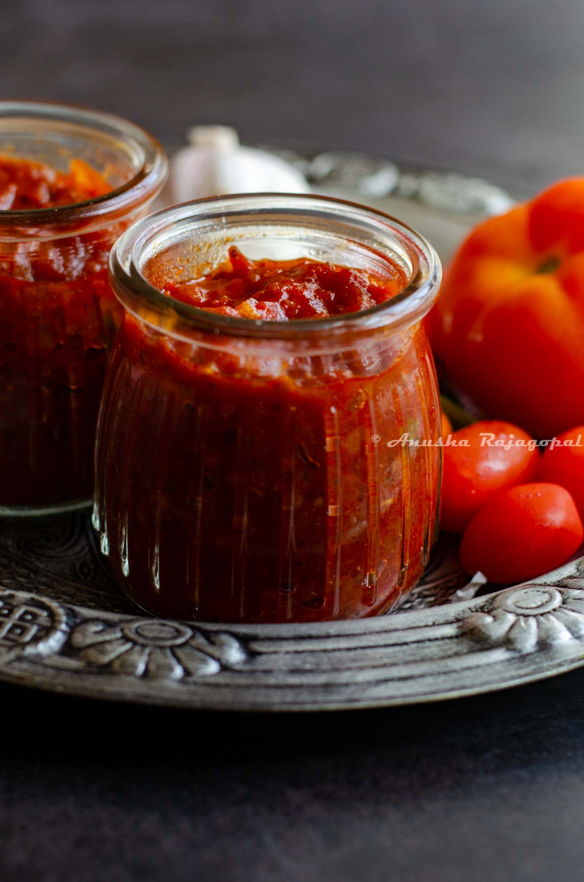 South Indian thakkali thokku- a tangy tomato relish in a glass jar with cherry tomatoes, garlic and curry leaves all presented in a rustic platter