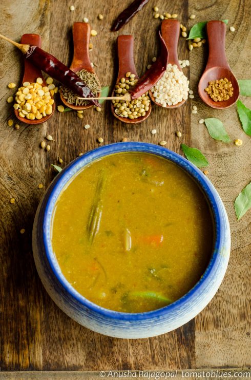 Kerala sambar served in a white and blue bowl placed over a wooden board. Spices in spoons kept at the background.