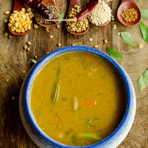 Kerala sambar placed on a wooden board with spices on small spoons in the background