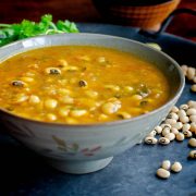 Black eyed peas curry served in a grey bowl placed on a blackish gray tray with scattered black eyed peas and cilantro at the background