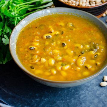Black eyed peas curry served in a grey bowl placed on a blackish gray tray with scattered black eyed peas and cilantro at the background