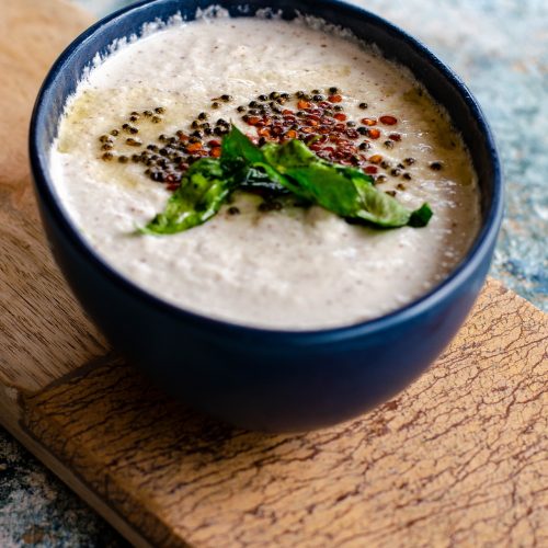 Salavai Chutney- South indian style vegan dip for Idli, dosa served in a blue bowl placed on a beige cheese board on a cement like backdrop.