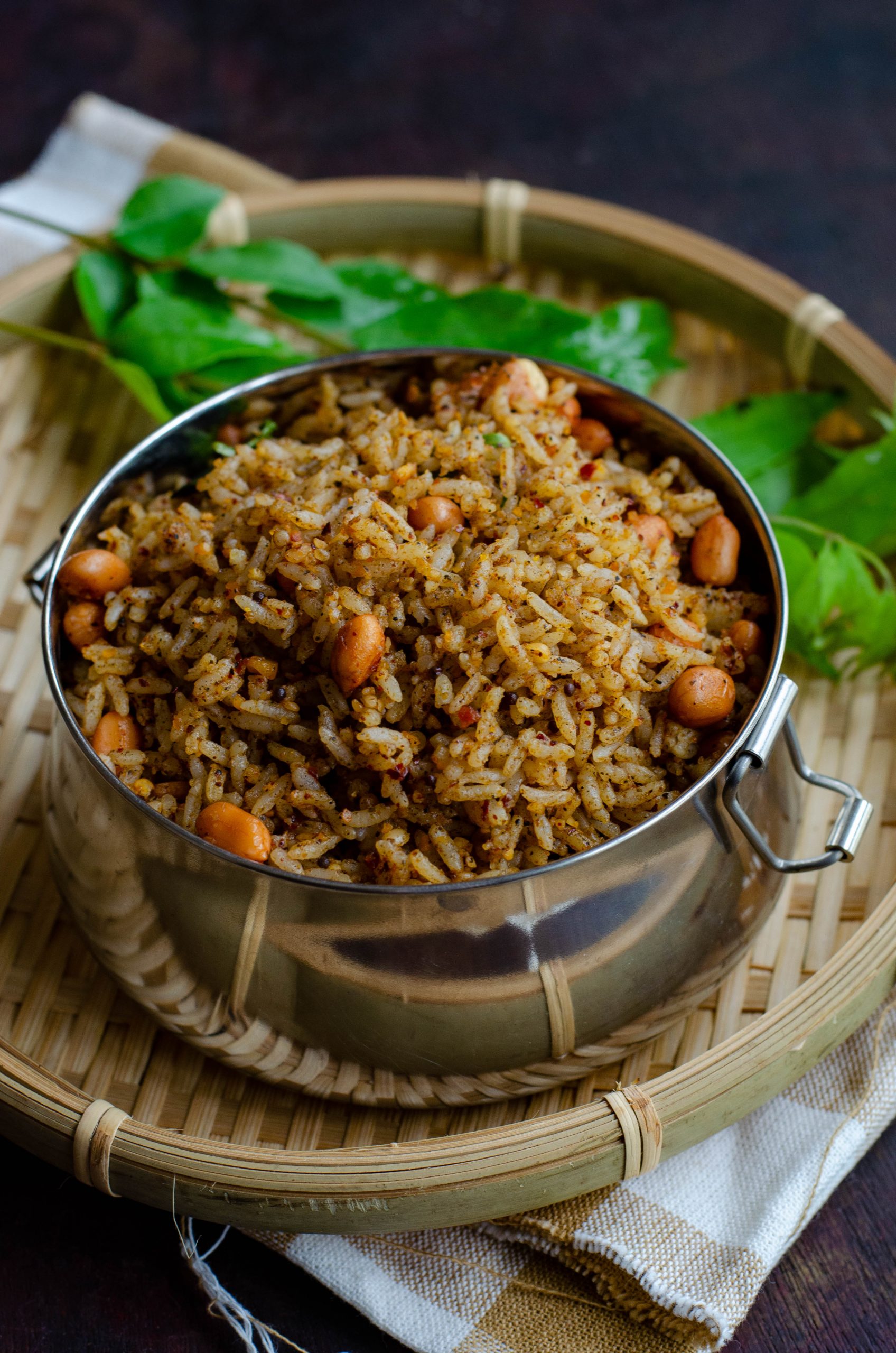 Ellu sadam- A simple vegan rice-based dish made with a sesame seeds based spice mix, served in a tiffin box placed on a bamboo basket against a brown backdrop.