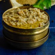 Thinai Ven Pongal served in a brass box with ghee on the top. Curry leaves and millet in a winnow as a backdrop.