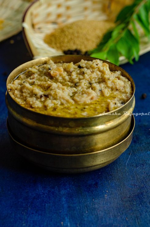 Thinai Ven Pongal served in a brass box with ghee on the top. Curry leaves and millet in a winnow as a backdrop.