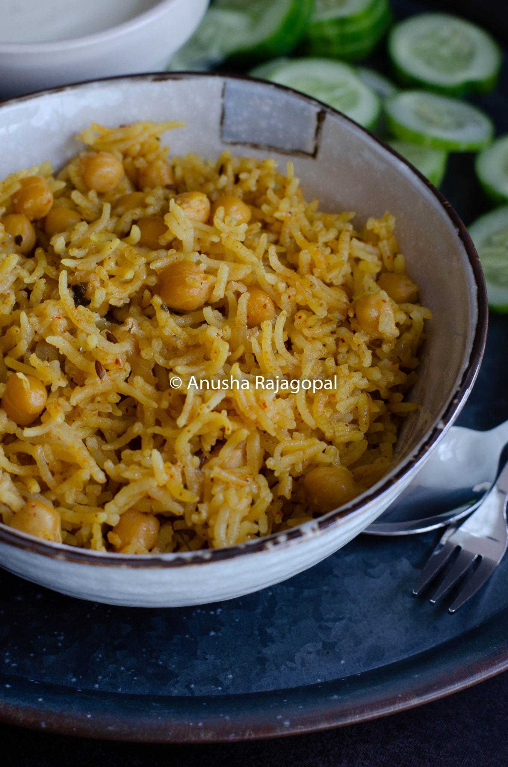 chana pulao in mealthy served in a beige bowl with cukes and raita.