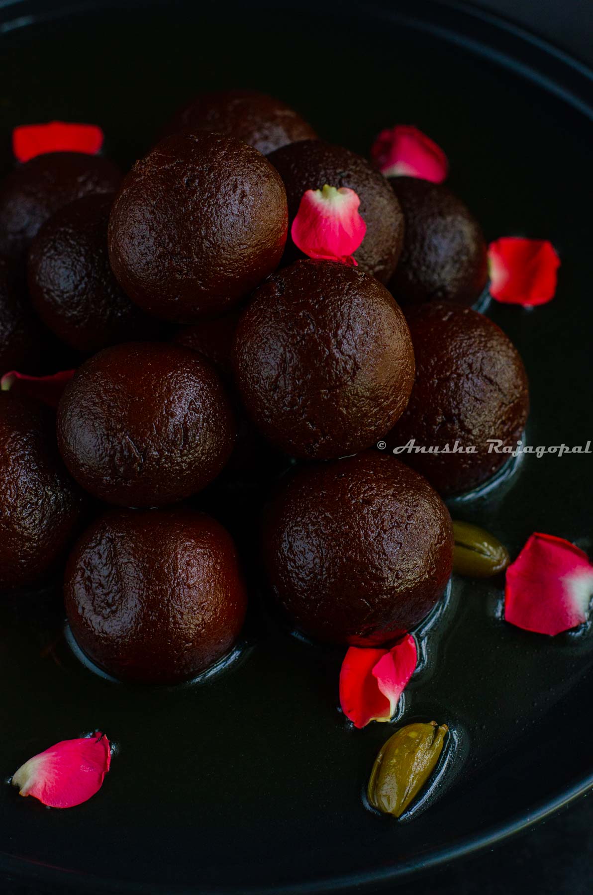 juicy black jamuns stacked and served on a black plate. Garnished with rose petals.