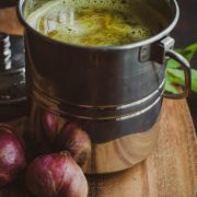 Onion rasam served in a stainless steel handled container placed on a wooden board