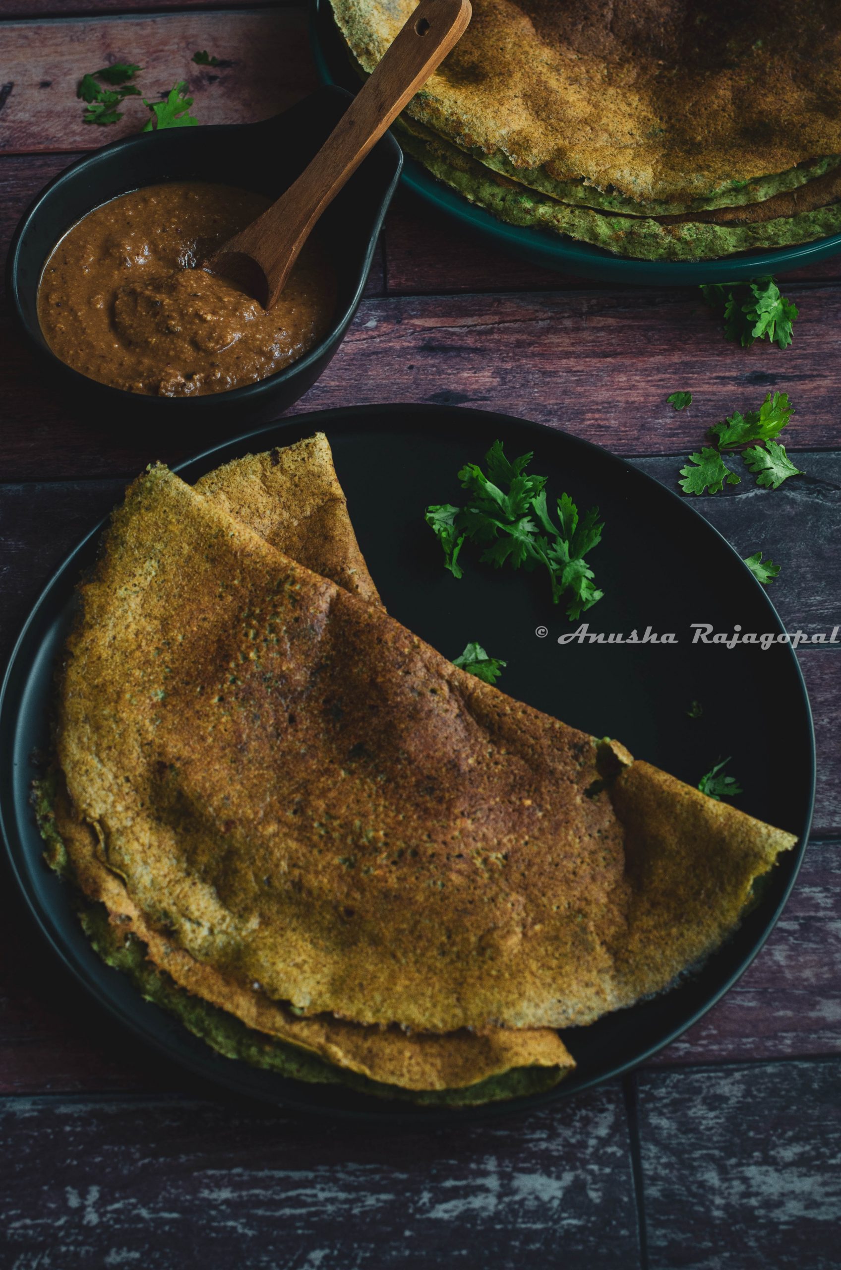 pesarattu- high protein moong beans dosa served on a black plate placed on a table.