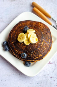 vegan banana oatmeal pancakes stacked and served on a white square plate. Banana and blueberries as toppings