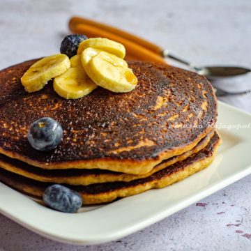 vegan banana oatmeal pancakes stacked and served on a white square plate. Banana and blueberries as toppings