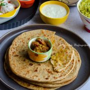 Gobi ke Paratha- Indian style cauliflower stuffed flatbreads served with mixed pickles placed in a small white and green dip bowl, placed on the top.