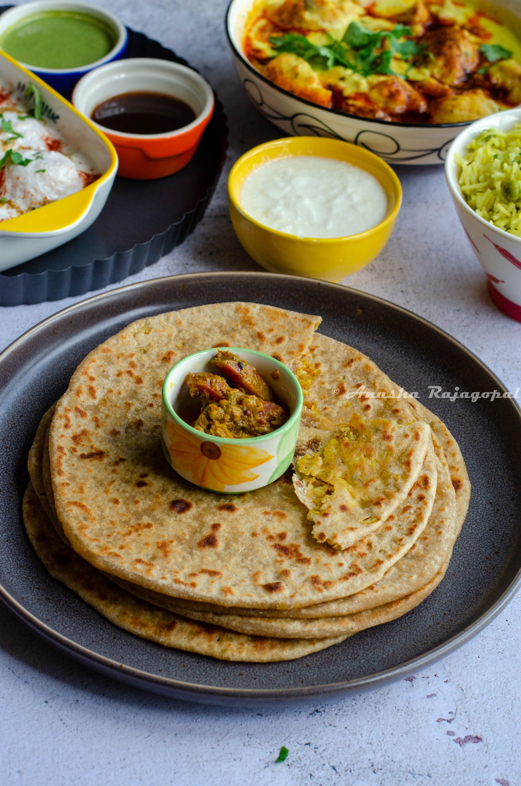Gobi ke Paratha- Indian style cauliflower stuffed flatbreads served with mixed pickles placed in a small white and green dip bowl, placed on the top.
