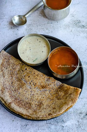 Ragi dosa served with coconut chutney and sambar on a black plate