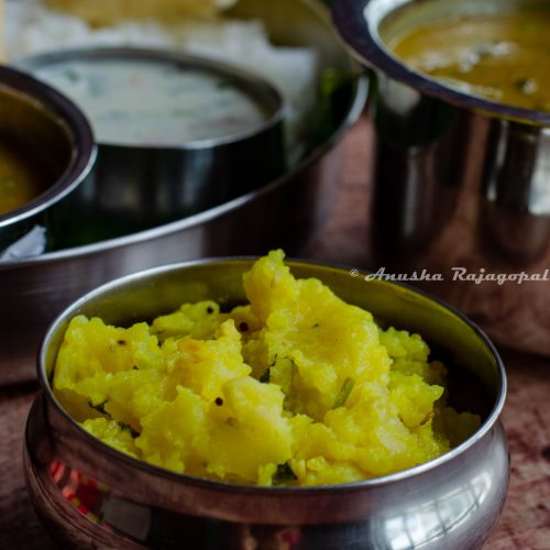 potato podimas served in a steel bowl with a full South Indian meal at the background