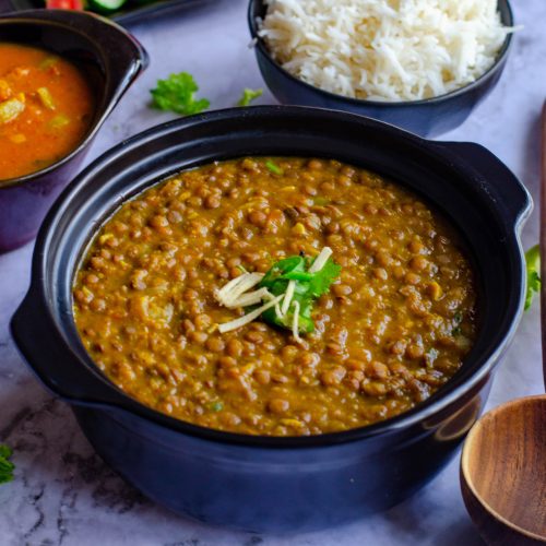 Instant pot whole masoor dal served in a black bowl with steamed rice and salad
