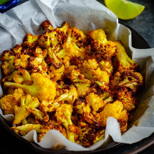 mexican air fryer caulilflower served in a tray with a mint dipping sauce and lemon wedges